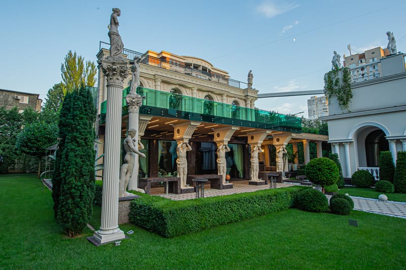 Grădina MiaDora cu alei pavate, statui pe coloane și la apus